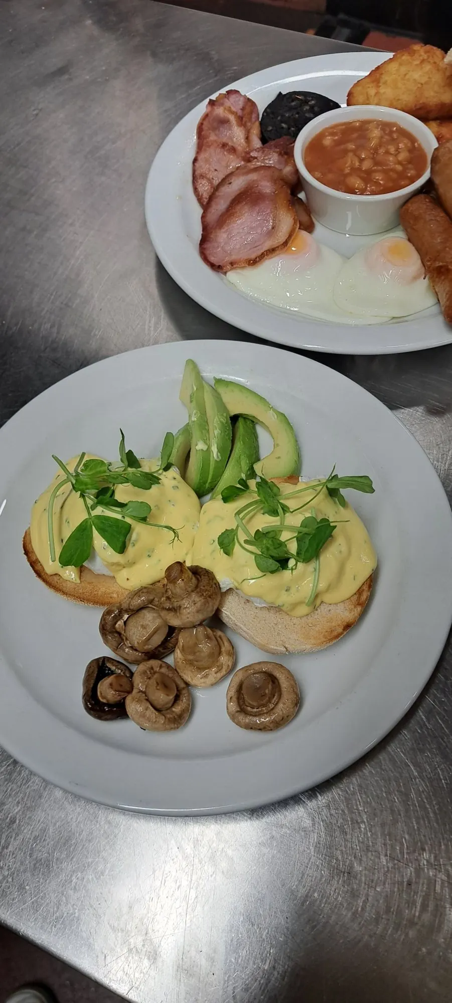 Eggs benedict with avocado and mushrooms beside a cooked breakfast